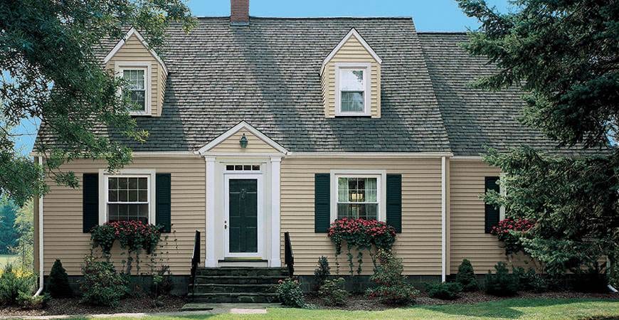 Siding installation on a classic two-story colonial home with tan vinyl siding and white trim