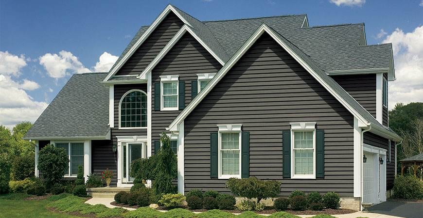 Siding installation completed on a two-story farmhouse-style home with dark olive green vinyl siding