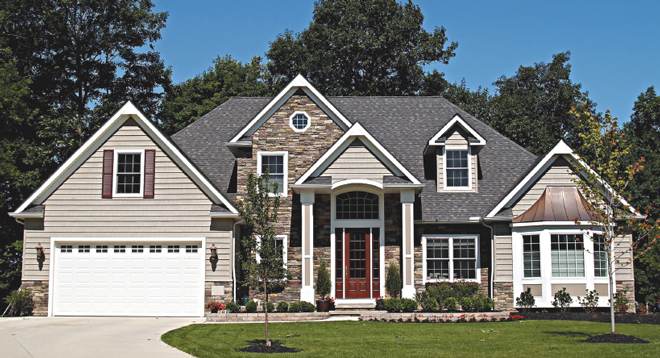 Siding installation on a craftsman-style home featuring mixed stone and beige vinyl siding with attached garage